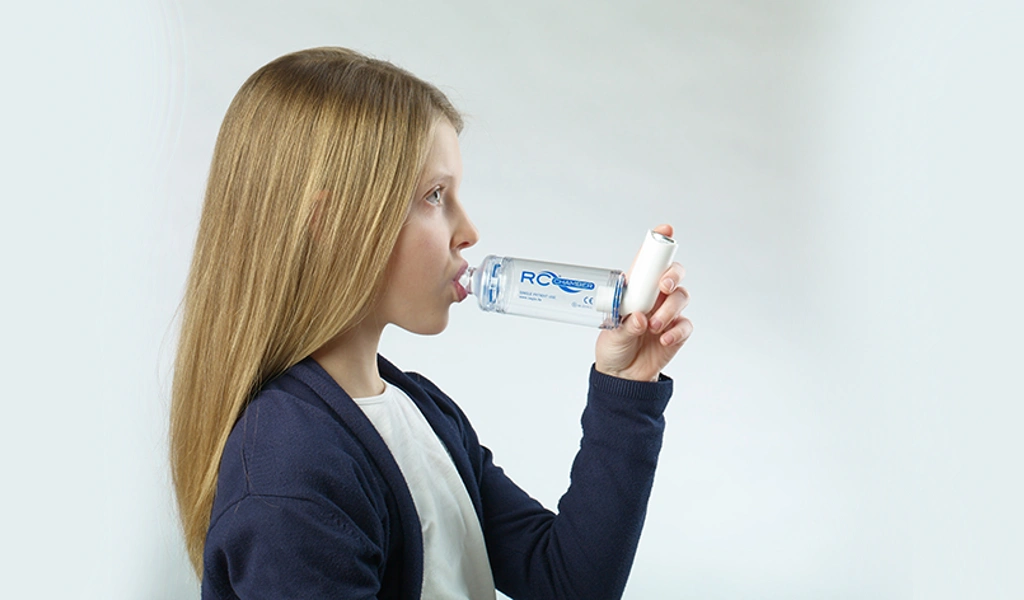 Ein blondes Mädchen verwendet eine Inhalierhilfe, um ihr Dosieraerosol zu inhalieren.