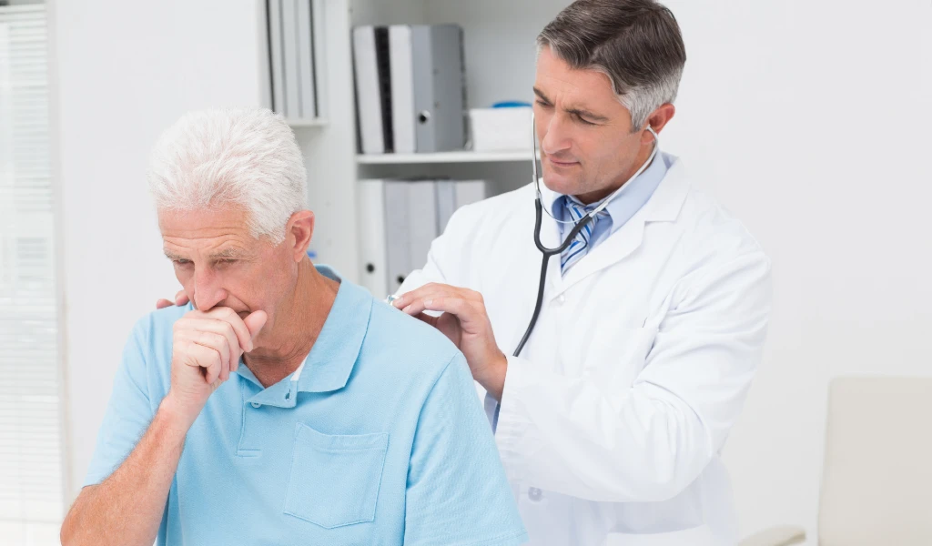 Ein Arzt untersucht einen hustenden älteren Mann mit einem Stethoskop.