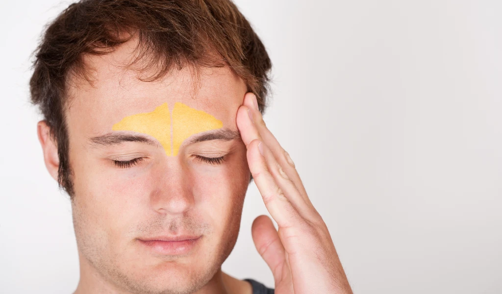 Mann mit geschlossenen Augen berührt seine Schläfe, gelbe Markierung auf der Stirn.