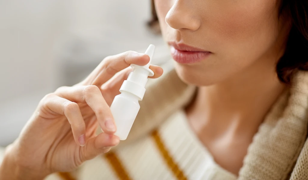 Nahaufnahme einer Frau, die ein Nasenspray-Fläschchen an ihre Nase hält.
