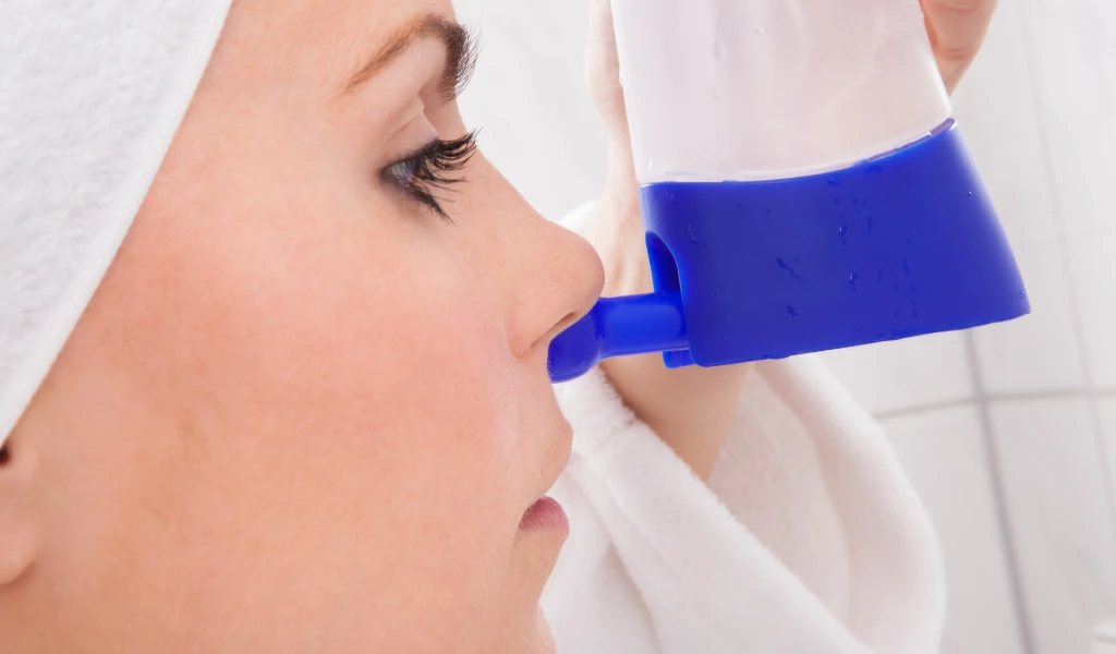 Seitenansicht einer Frau, die eine blaue Nasenspülkanne verwendet.