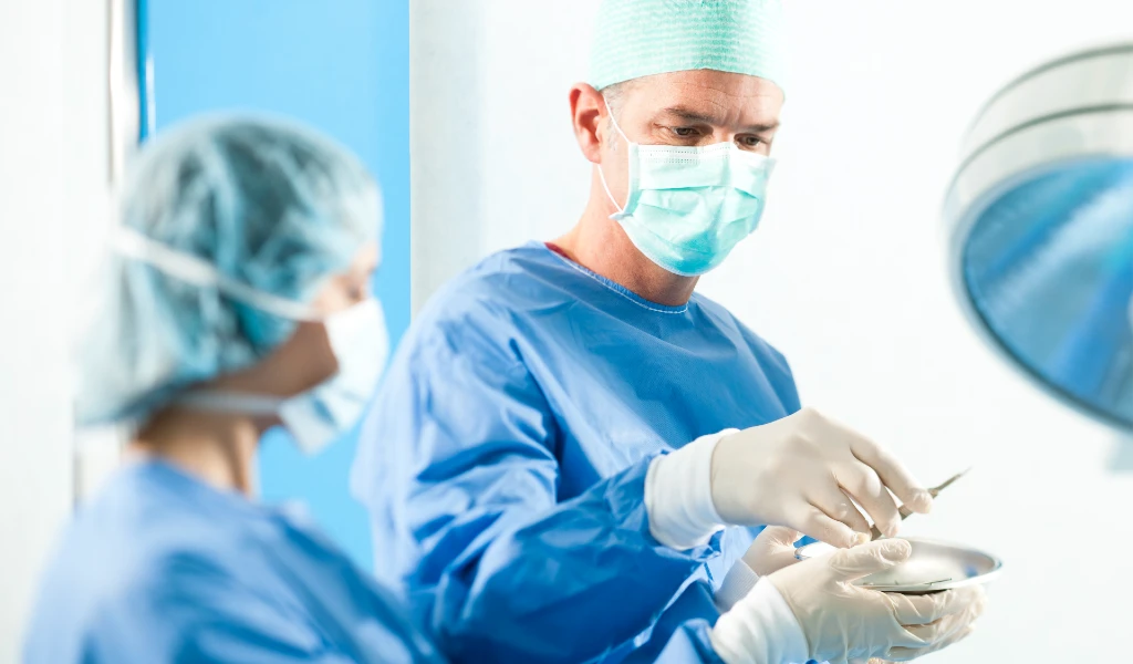 Zwei Chirurgen in blauer OP-Kleidung, Masken und Hauben bei der Arbeit im Operationssaal.