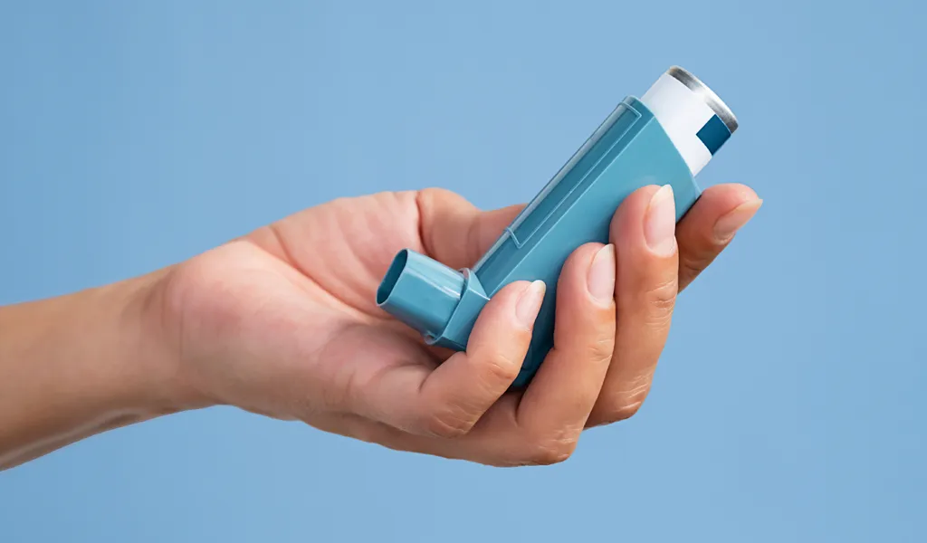 Hand hält einen blauen Asthmainhalator vor hellblauem Hintergrund.