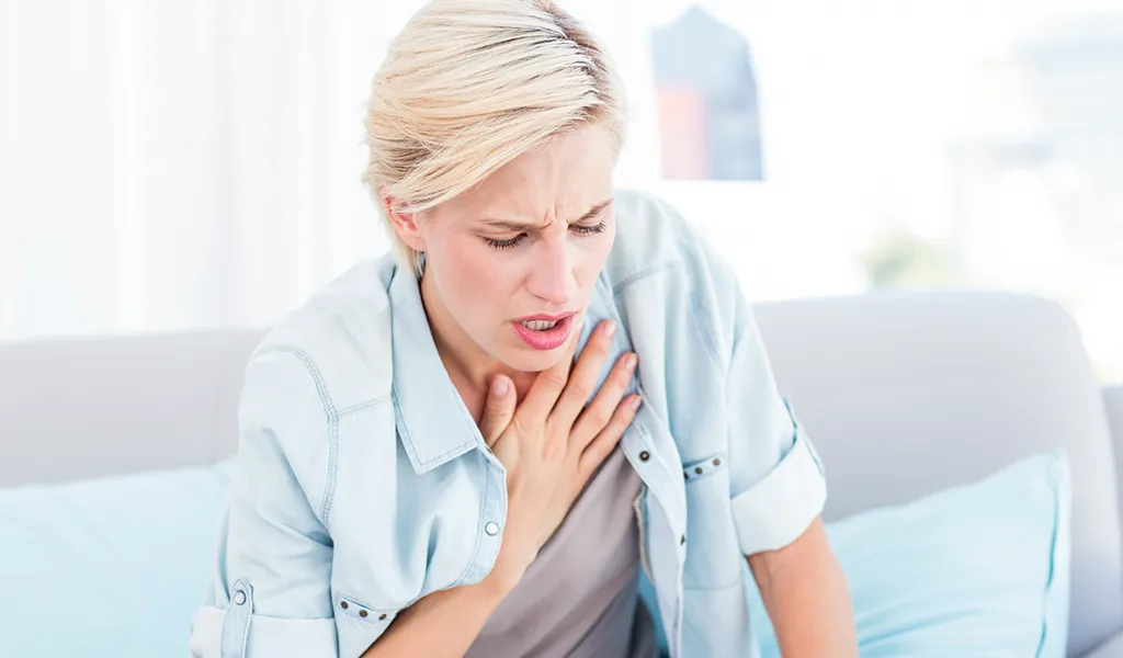 Blonde Frau mit Atembeschwerden hält sich Hand an den Brustkorb