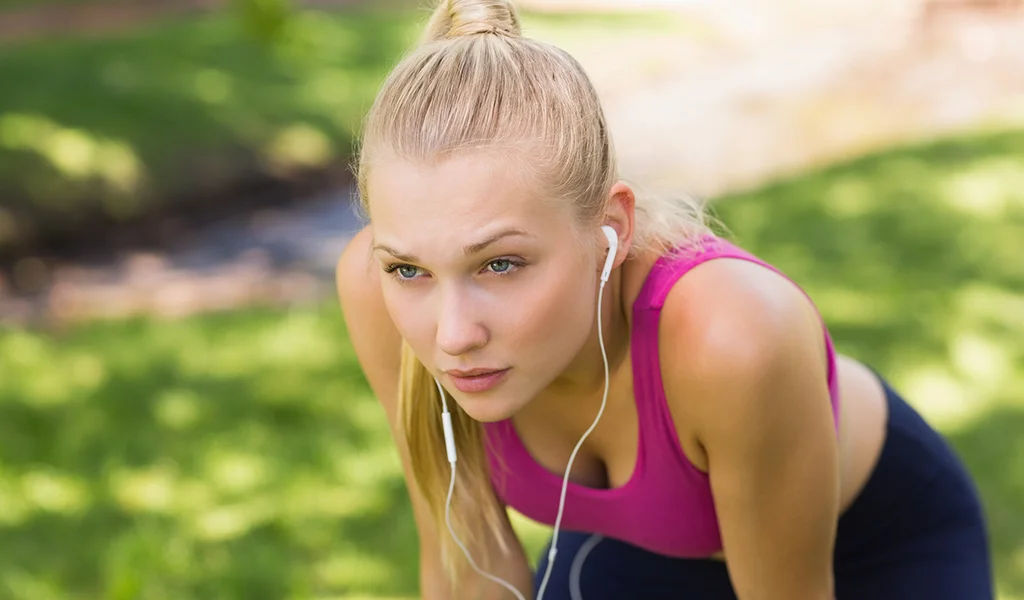 Frau in einem rosa Tanktop, mit Kopfhörern, nach vorne gebeugt im Freien, mit konzentriertem Blick.