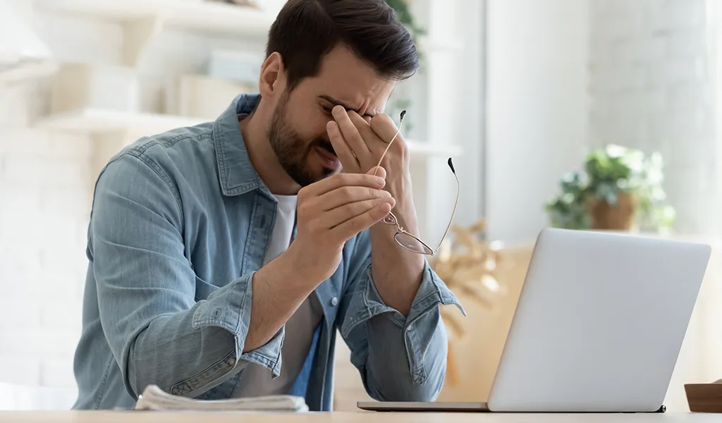 Junger Mann mit Brille reibt sich die müden Augen