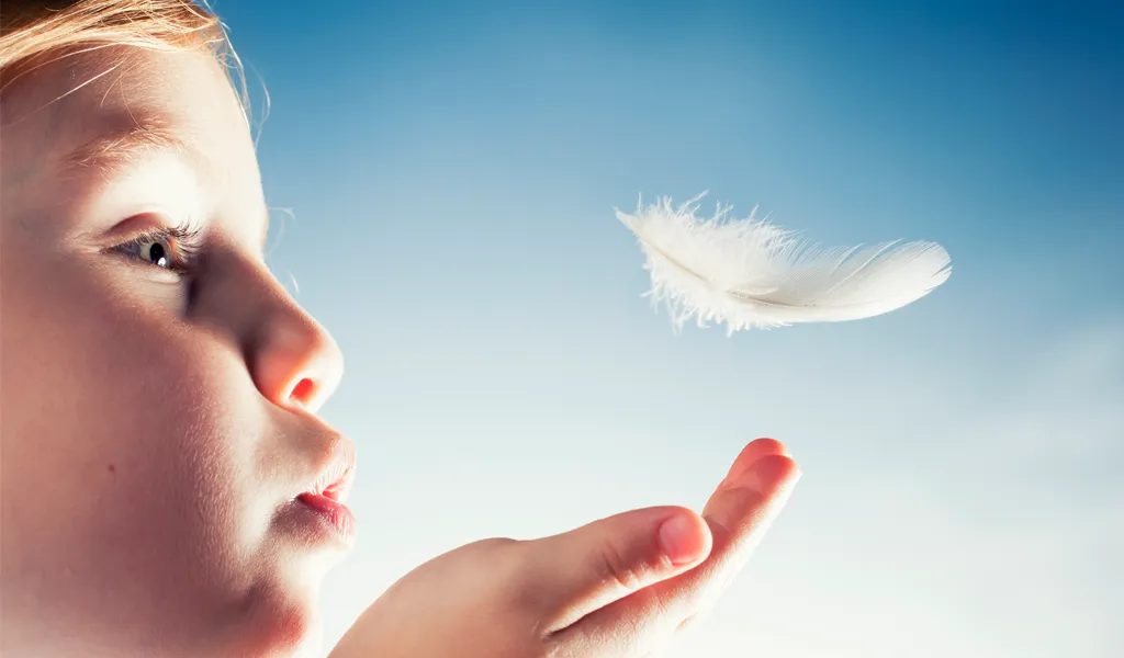 Kind spitzt die Lippen und bläst eine Feder in die Luft