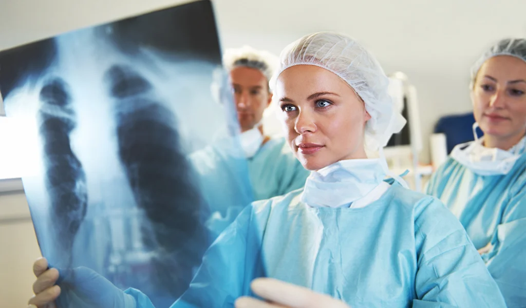 Ein medizinisches Team in OP-Kleidung untersucht in einer Klinik eine Röntgenaufnahme des Brustkorbs.